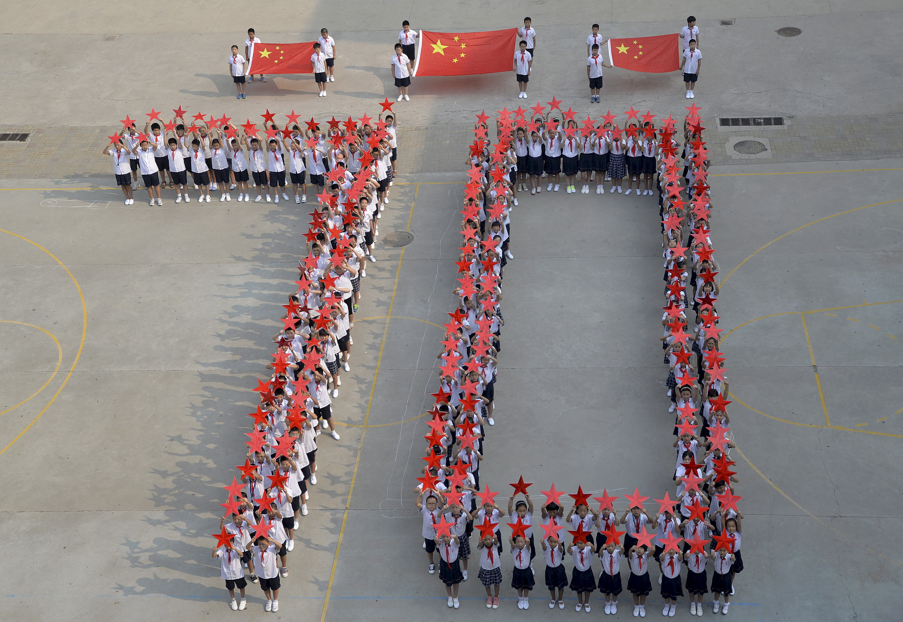 Студенты позируют с китайскими национальными флагами и красными звездами в рамках подготовки к параду 31 августа 2015 года